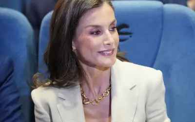 La reina Letizia, con un traje beige y un collar dorado, sonríe mientras asiste a un evento.