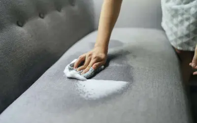 A hand with a soapy cloth gently cleans a grey couch cushion, showing how to wash couch cushion covers for a fresh look.