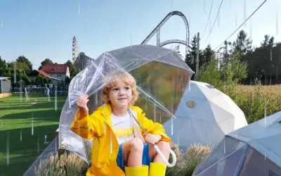 Chłopiec w żółtej kurtce i kaloszach pod przezroczystym parasolem, w tle rollercoaster. Czy Energylandia jest otwarta w deszcz?
