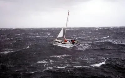 Un voilier affronte une mer agitée, sa voile blanche tendue. La mise à la cape est une manœuvre de survie face aux éléments déchaînés.