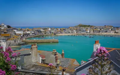 En solig vy över St Ives med turkost vatten, båtar och hus. Blommor i förgrunden ger en somrig känsla.