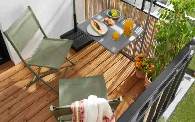Idéal pour aménager un petit balcon en longueur : deux chaises pliantes vertes, une table avec fruits et jus, et des plantes.