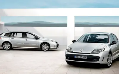 Dwa srebrne Renault Laguna 3 2.0 dCi: kombi i sedan, stojące na nowoczesnym placu z widokiem na góry.
