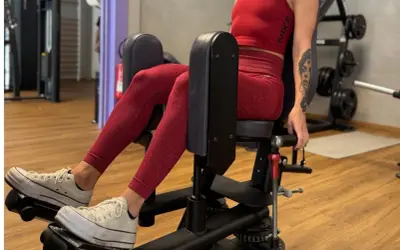 Femme en tenue de sport rouge travaillant son abducteur muscle sur une machine de musculation.