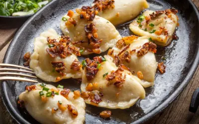 Pyszne pierogi z mięsem mielonym, okraszone skwarkami i szczypiorkiem, podane na żeliwnej patelni.