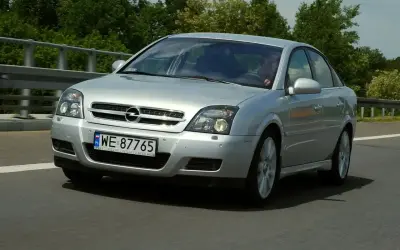 Srebrny Opel Vectra jedzie po drodze, za nim zielone drzewa.