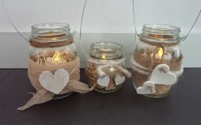 Tre vasetti lanterne fai da te decorati con cuori e spago, con candele accese all'interno per un'atmosfera calda.