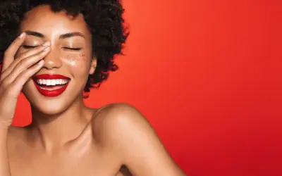 Une femme rit, la main sur le visage, avec un rouge à lèvres éclatant. Quelle couleur de rouge à lèvres !