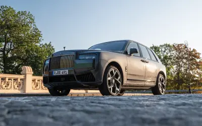 Elegancki Rolls-Royce Cullinan na kamienistej drodze, z grillem i charakterystyczną figurką na masce.