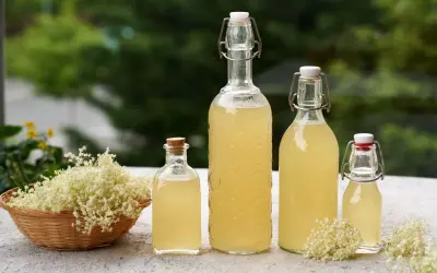 Fiori di sambuco in un cesto e bottiglie di sciroppo fatto in casa. Freschezza estiva da gustare.