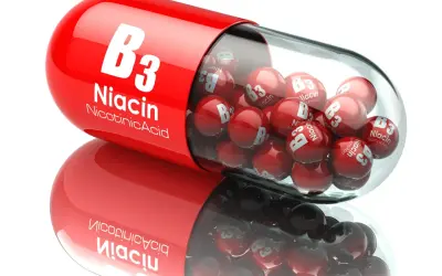 Czerwona kapsułka wypełniona małymi kulkami z napisem "Niacin B3". To niacynobaza w pigułce.
