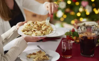 Rodzina przy wigilijnym stole dzieli się pysznymi pierogami. W tle choinka, a na stole kompot. Idealne wierszyki na polaznika!