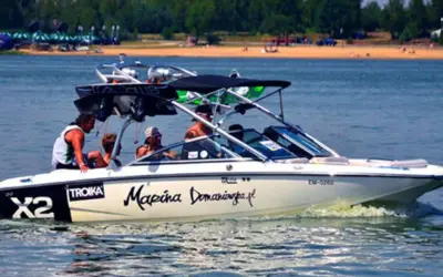 Łódź motorowa z pasażerami płynie po wodzie, tworząc pianę. Na burcie widnieje napis "Marina Domaniewska".