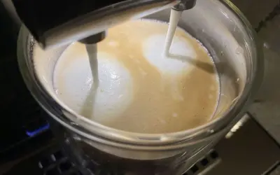 Mleko wylewa się z dyszy ekspresu DeLonghi, tworząc piankę na kawie. Niestety, ekspres DeLonghi nie spienia mleka tak, jak powinien.