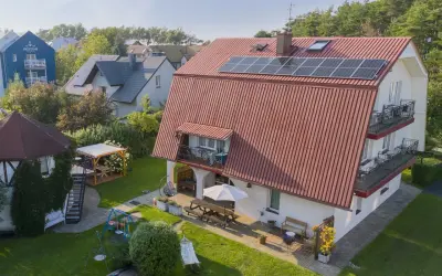 Idealne chłopy noclegi przy plaży: dom z ogrodem, placem zabaw, hamakiem i grillem. W tle widać inne budynki i las.