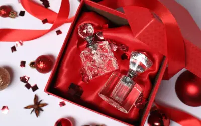 Elegancki prezent na urodziny dla żony: dwa kryształowe flakoniki perfum w czerwonym pudełku, ozdobione wstążką i błyszczącym konfetti.