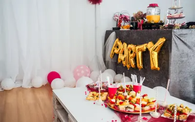 Złote balony z napisem "PARTY" i przekąski na stole tworzą atmosferę wieczoru panieńskiego w domu.