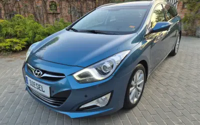 Niebieski Hyundai i40 1.7 CRDi na podjeździe z kostki brukowej, z tyłu ceglany mur porośnięty bluszczem.