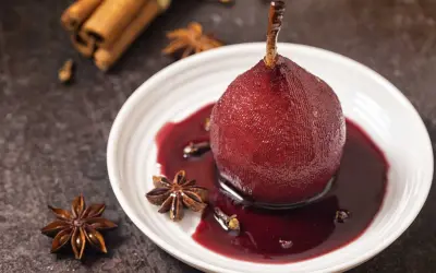 Peras al vino tinto, cocidas con especias como anís estrellado y canela, servidas en un plato blanco con su sirope.