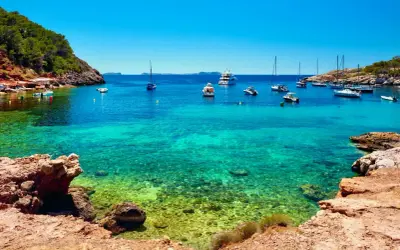 Aguas cristalinas en cala salinas, con barcos anclados y una costa rocosa y verde.