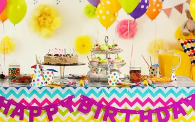 Kolorowy stół z tortem, babeczkami i słodyczami czeka na imieniny Gosi. Balony i girlanda "Happy Birthday" tworzą radosną atmosferę.