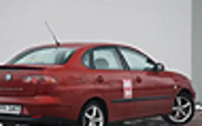 Czerwony Seat Cordoba z naklejką na drzwiach, zaparkowany na zewnątrz.