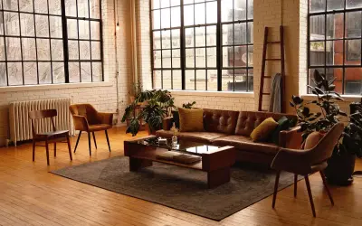 Przytulny salon w stylu loft aranżacje. Brązowa skórzana kanapa, drewniane meble i duże okna tworzą ciepłą atmosferę.