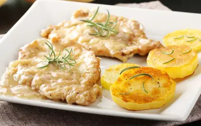 Two breaded chicken cutlets in creamy sauce with rosemary, served with pan-fried potato slices.