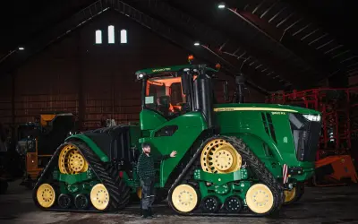Man bredvid en stor grön John Deere-traktor i en lada. Frågan "hur länge håller diesel" kan vara relevant för denna maskin.