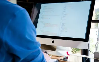 Programista w niebieskiej bluzie pochyla się nad monitorem z kodem.