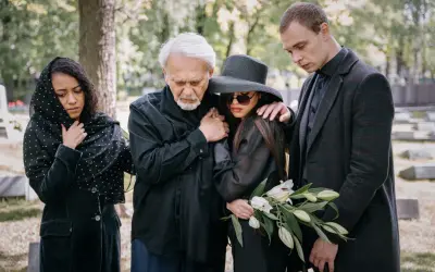 Smutna rodzina na cmentarzu. Elegancki ubiór damski na pogrzebie latem, z welurową marynarką i kapeluszem.