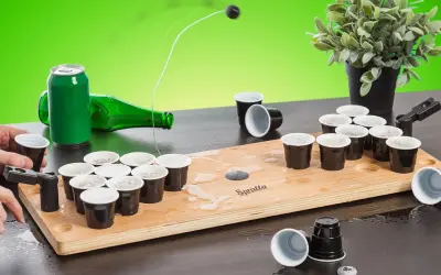 En rolig lekar fest vuxna inomhus med beer pong-spel. En boll flyger mot muggarna på träplattan.