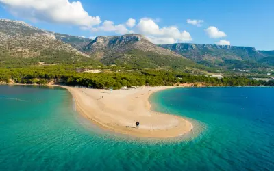 Spiaggia a forma di lingua di sabbia dorata, bagnata da acque cristalline, con montagne verdi sullo sfondo. Un angolo di paradiso in **Croazia mare**.