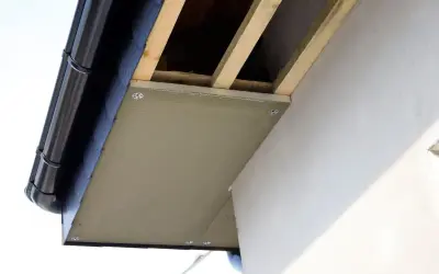 Montaż podprzybitki pod okapem dachu, widoczne drewniane krokwie i rynna.