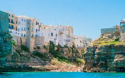 La famosa spiaggia di Polignano a Mare, con case bianche aggrappate alle scogliere e bagnanti che si godono il mare cristallino.