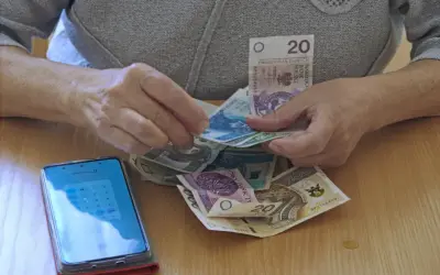Dłonie liczą pieniądze, obok leży smartfon z kalkulatorem. Czy to dodatek pielęgnacyjny z ZUS, komu przysługuje?