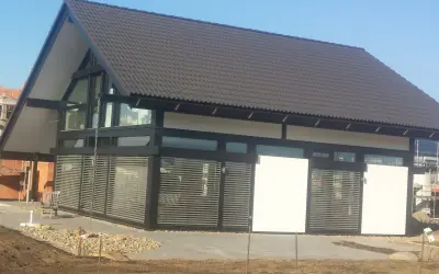 Nowoczesny dom z dużymi oknami dźwiękoszczelnymi, zadaszeniem i żaluzjami.