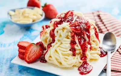 Ein köstliches Spaghetti-Eis-Dessert mit Erdbeersauce und frischen Erdbeeren, garniert mit weißer Schokolade.