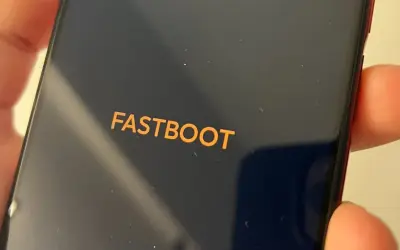 Pomarańczowy napis FASTBOOT na ciemnym ekranie telefonu, trzymanego w dłoni.