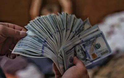 Dłonie trzymają wachlarz banknotów 100-dolarowych, sugerując pranie pieniędzy.