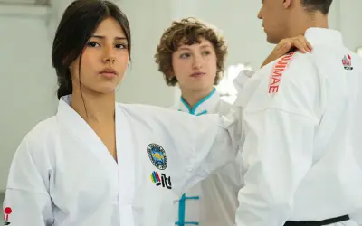 Trójka młodych ludzi w białych strojach do taekwondo, jednej z najpopularniejszych sztuk walki, ćwiczy w sali treningowej.