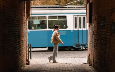 Una ragazza cammina in un vicolo, un tram blu sfreccia sullo sfondo. Una foto vedo non vedo che cattura un momento fugace.