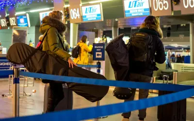 Osoby z bagażem sportowym, w tym futerałem na instrument, czekają na odprawę na lotnisku. Idealny bagaż sportowy Ryanair na podróż.