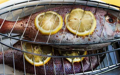 Två hela fiskar ligger på ett grillgaller, toppade med citronskivor. Snart är det dags att grilla fisk!
