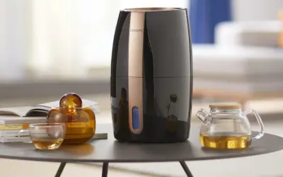 Elegancki czarny nawilżacz Philips z miedzianym akcentem. Obok szklanka z herbatą, bursztynowa buteleczka i mały dzbanuszek. Czy do każdego nawilżacza można wlać olejek?