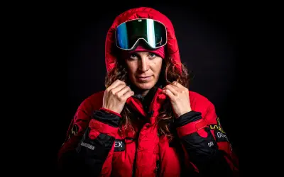 Tamara Lunger, bereit für extreme Bedingungen, zieht ihre rote Kapuze hoch. Ihre Skibrille spiegelt das Licht.