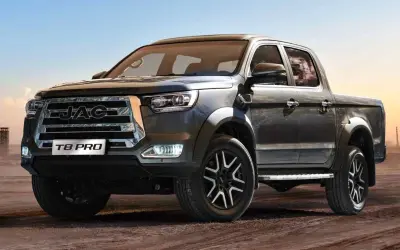 Ciemnoszary pickup JAC T8 PRO z chromowanym grillem i felgami stoi na piaszczystym podłożu.