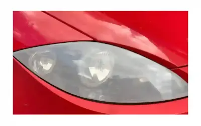 Gros plan sur un phare opaque de voiture rouge, reflétant le ciel.