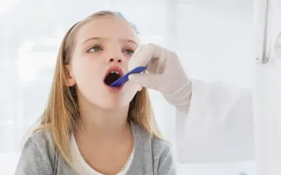 Niña con la boca abierta, examinada por un médico. Podría ser una consulta previa a una **operación amígdalas niños**.