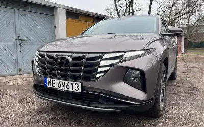 Szary Hyundai Tucson Hybrid z charakterystycznym grillem i światłami LED stoi przed garażami.